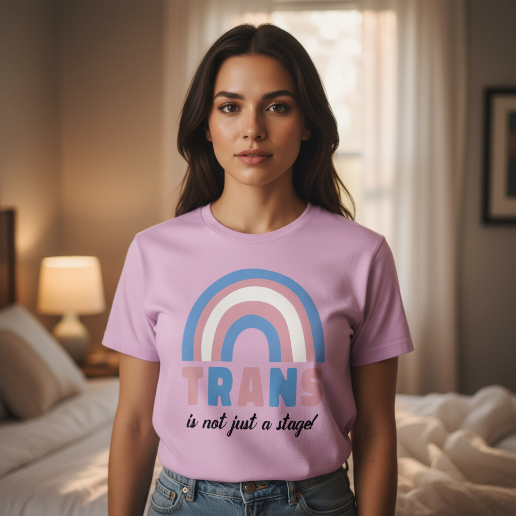 Lavender "Trans Is Not Just A Stage!" tee with trans pride rainbow, bold letters, worn by a person in a softly lit bedroom