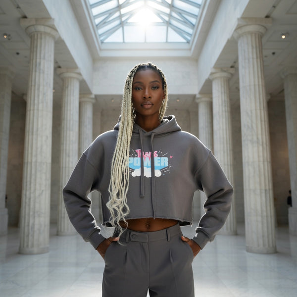 Trans Power Crop Hoodie and high-waisted pants, queer style, worn by a proud woman with blonde braids in a grand hall.