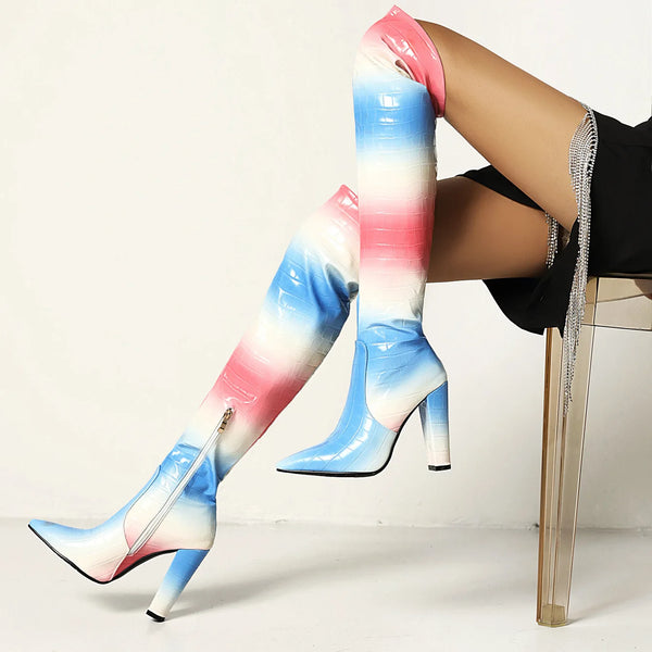 Trans pride knee-high crocodile-textured boots with pointed toes and high heels, worn by a model