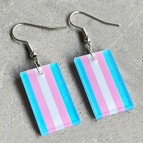 Pair of rectangular transgender pride flag acrylic dangle earrings on a gray surface