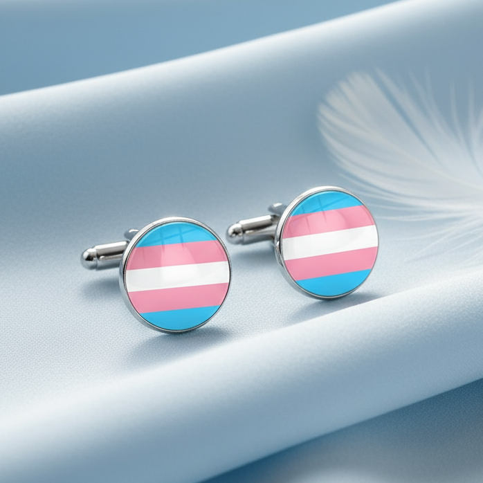 Pair of round transgender pride flag cufflinks resting on pale blue fabric