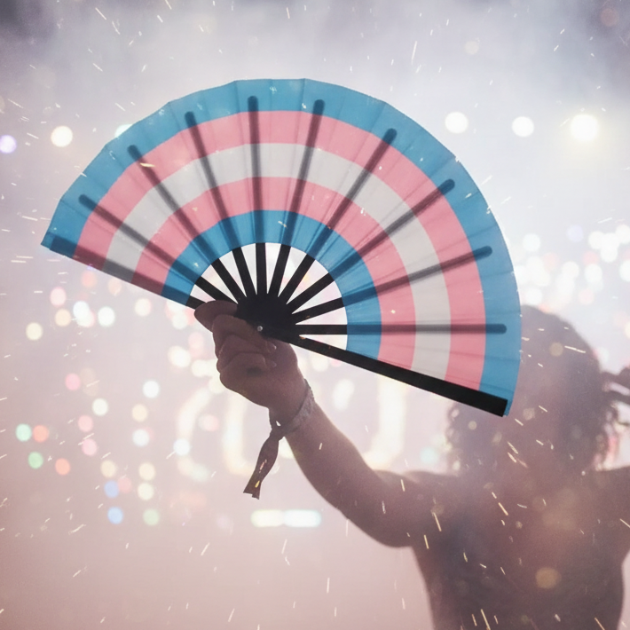 Open transgender pride folding fan held up by a silhouetted person at a light-filled event