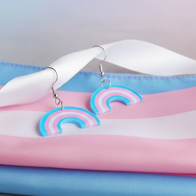 Pair of pink, blue, and white rainbow dangle earrings on a trans pride flag