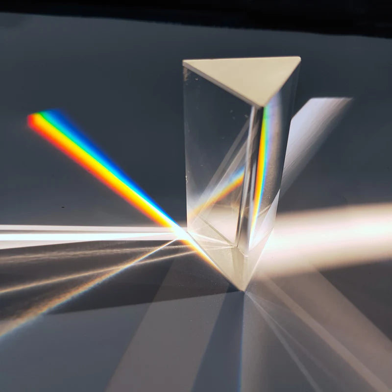 Clear triangular prism standing on a dark surface, casting a vivid rainbow beam and light rays