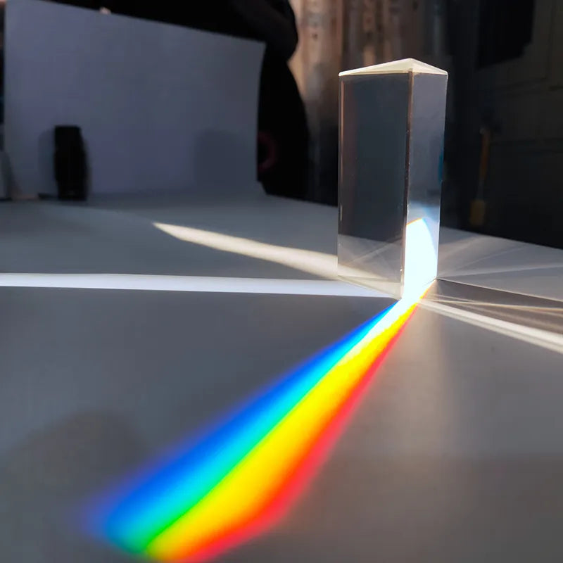 Clear triangular prism standing on a table, casting a vivid rainbow beam in sunlight