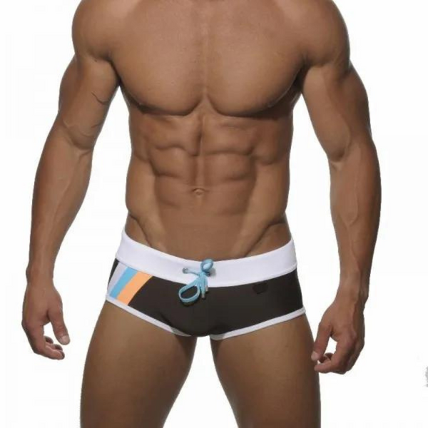 swimwear for gays: Muscular person in black square cut swim trunks with orange and blue stripes stands by the pool