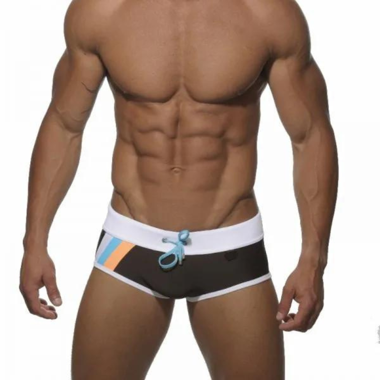 swimwear for gays: Muscular person in black square cut swim trunks with orange and blue stripes stands by the pool