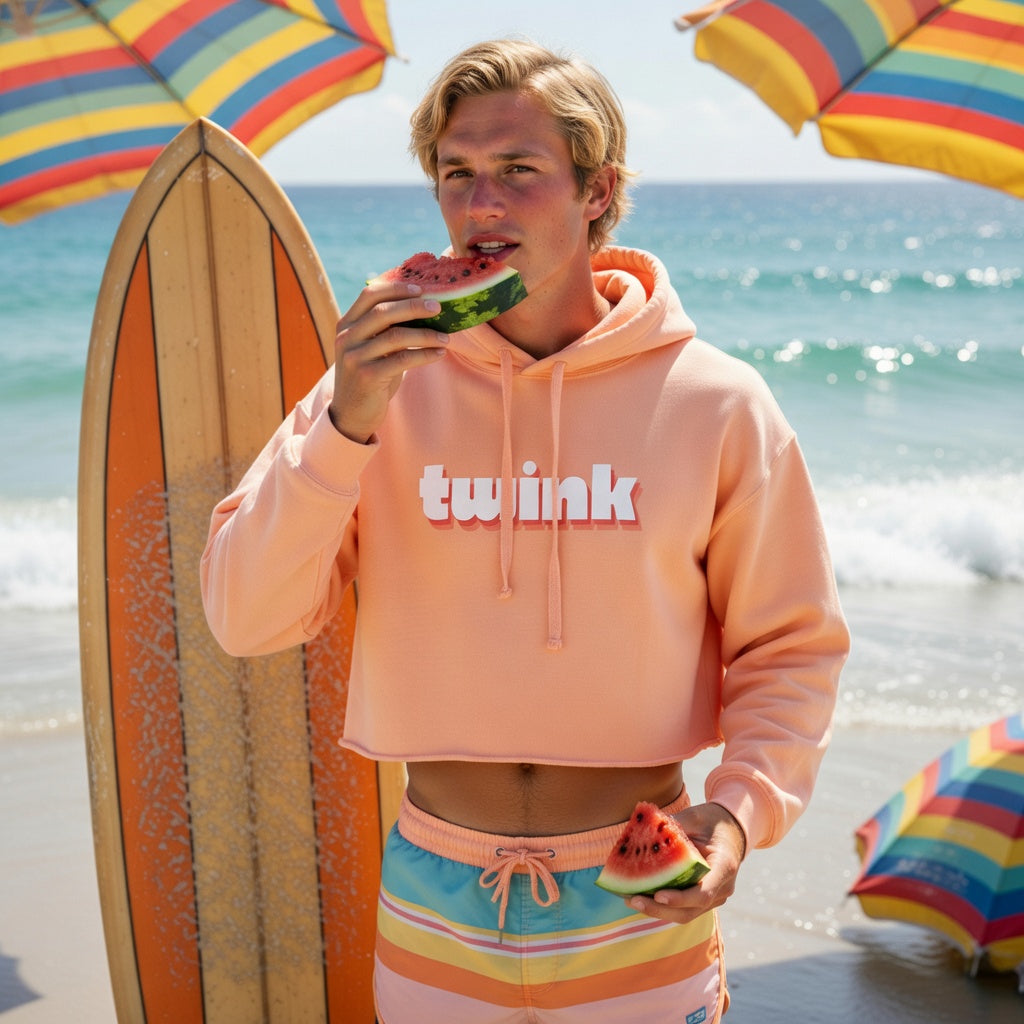 Twink Crop Hoodie with rainbow swim trunks on a queer beachgoer, bright umbrellas and surfboard, vibing by ocean waves.