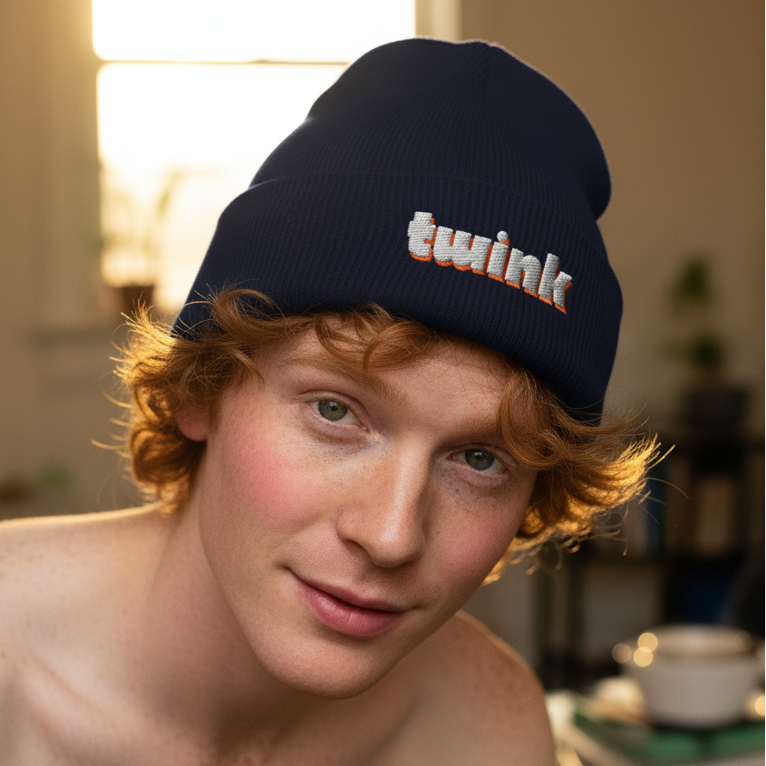 Navy Twink Cuffed Beanie with "twink" embroidered, worn by a red-haired, fair-skinned person, glows in warm window light
