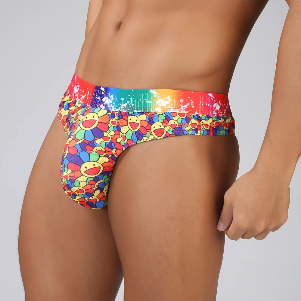 Close-up angled view of a model wearing colorful floral swim briefs with a rainbow waistband