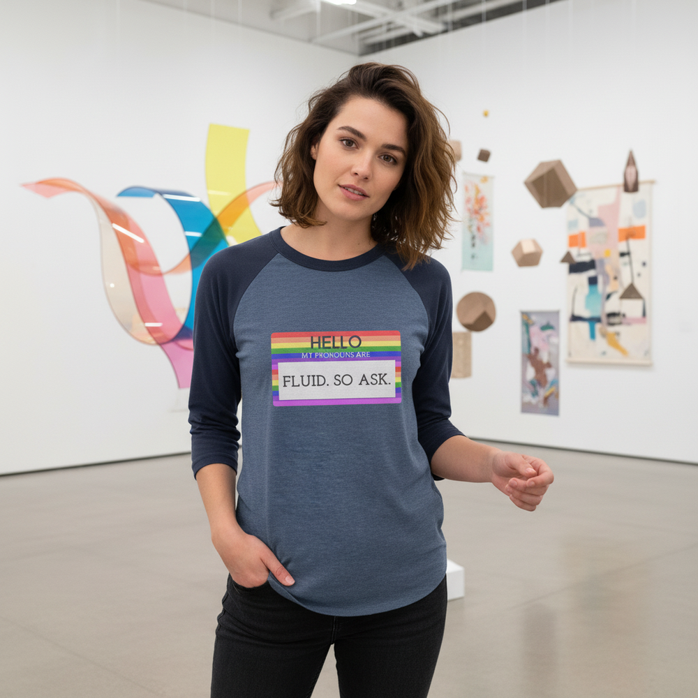 3/4 sleeve raglan shirt reads "Hello My Pronouns Are Fluid. So Ask." Wavy-haired woman in art gallery with colorful wall art.