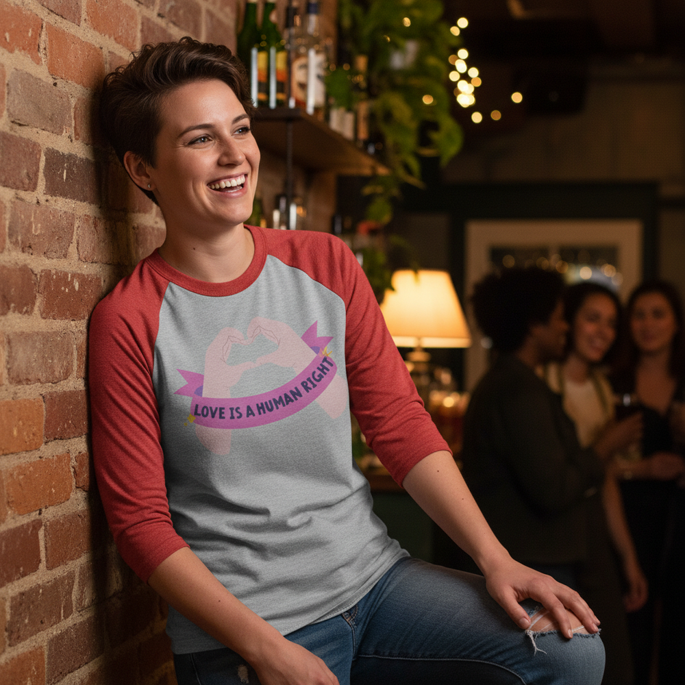3/4 sleeve raglan tee with gray and red sleeves, “Love Is A Human Right” slogan, heart hands graphic; cozy queer bar vibes.