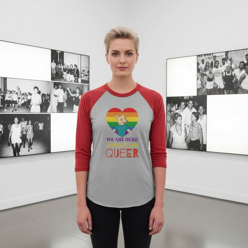 Front-facing model wearing a gray raglan shirt with red sleeves and a rainbow heart reading “WE ARE HERE AND WE ARE QUEER.”