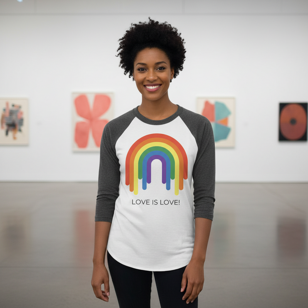 Rainbow 3/4 sleeve raglan tee with “LOVE IS LOVE!” graphic, worn by a smiling person in a bright, polished art gallery.