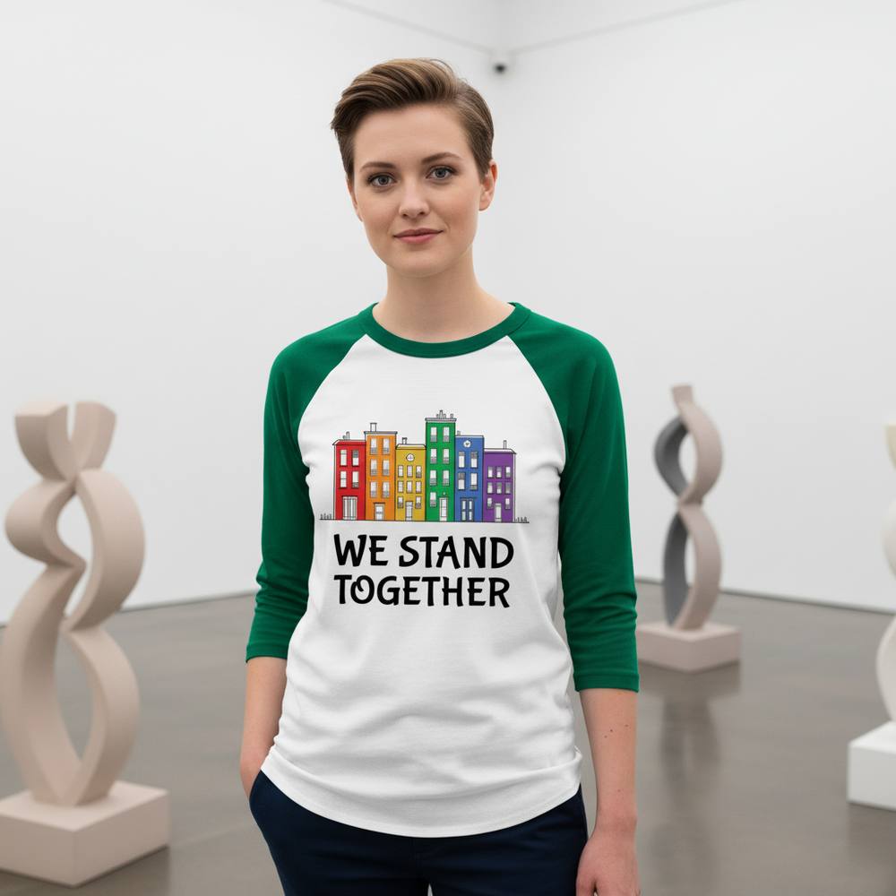 Person wearing a white raglan shirt with green sleeves, colorful buildings, and “WE STAND TOGETHER”