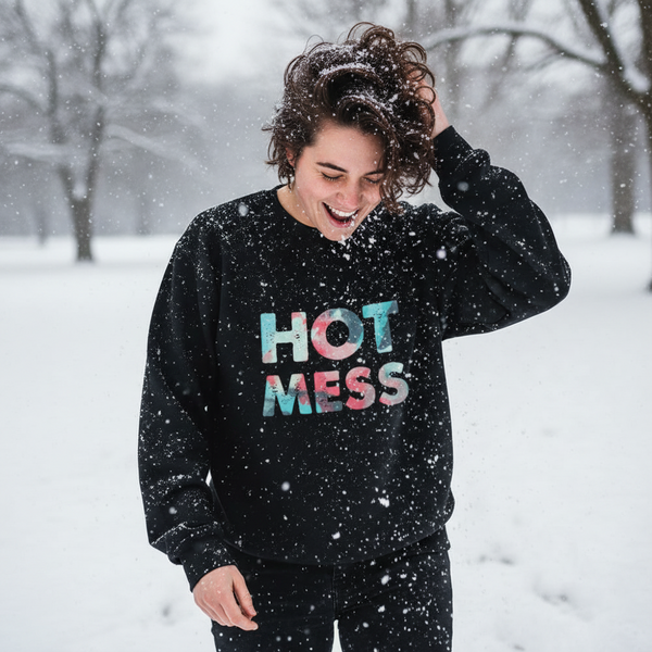 Person outdoors in falling snow wearing a black sweatshirt reading “HOT MESS”