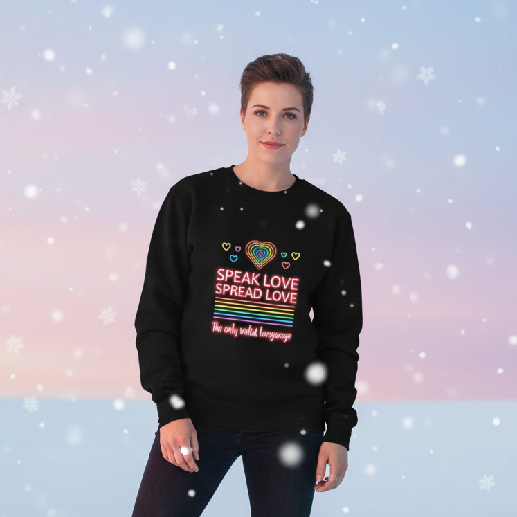 Person wearing the Speak Love Spread Love Unisex Sweatshirt, featuring a neon rainbow heart and multicolored lettering. Perfect for expressing pride and warmth, embodying joyful queer visibility and self-expression.