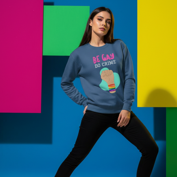 Model wearing a slate-blue sweatshirt reading “BE GAY DO CRIME” with a raised fist graphic
