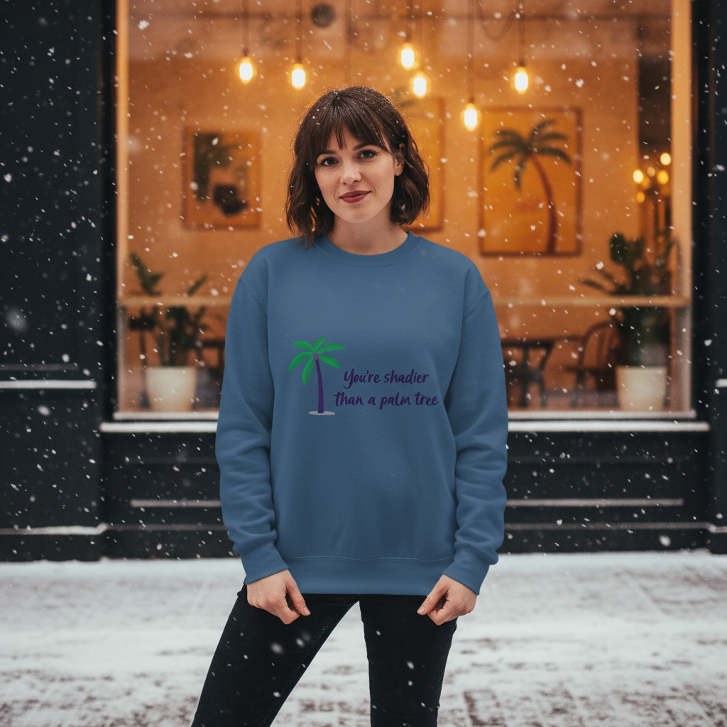 Young woman in the falling snow wearing the Shadier Than A Palm Tree Unisex Sweatshirt, showcasing queer empowerment and playful pride. The blue sweatshirt features a palm tree graphic and sassy text.