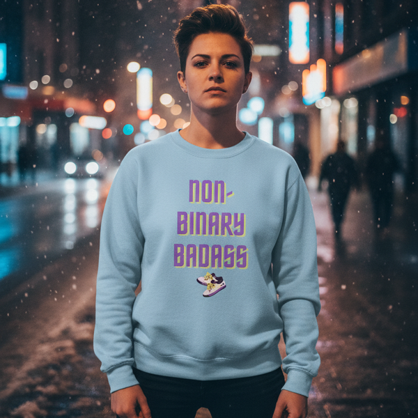 Front-facing person wearing a light blue sweatshirt reading “NON-BINARY BADASS” with a sneaker graphic