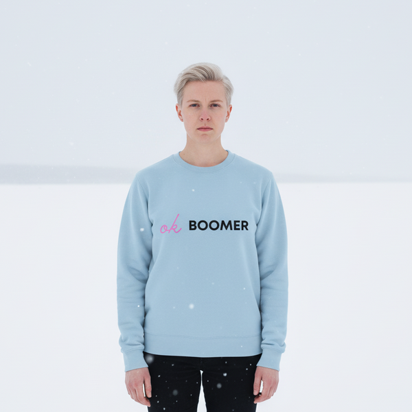 Front-facing person in falling snow wearing a light-blue sweatshirt reading “ok BOOMER”