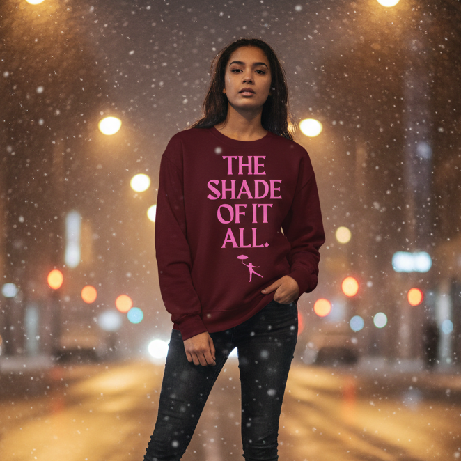 Model wearing a burgundy sweatshirt with pink “THE SHADE OF IT ALL” graphic