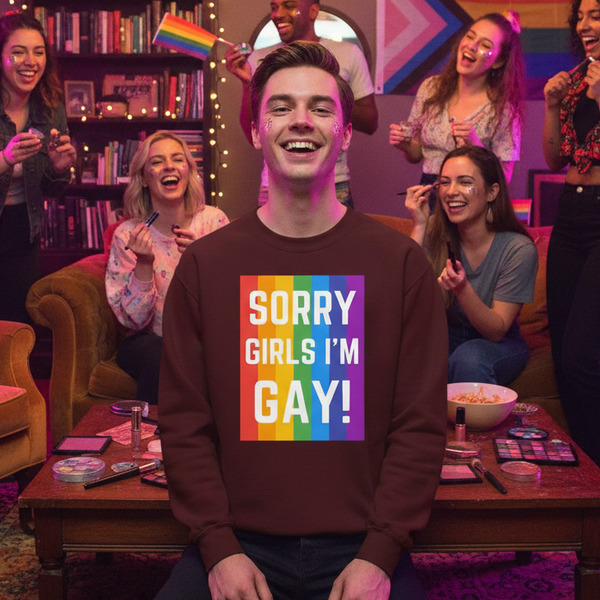 Smiling person wearing a brown sweatshirt reading “SORRY GIRLS I’M GAY!” with rainbow stripes