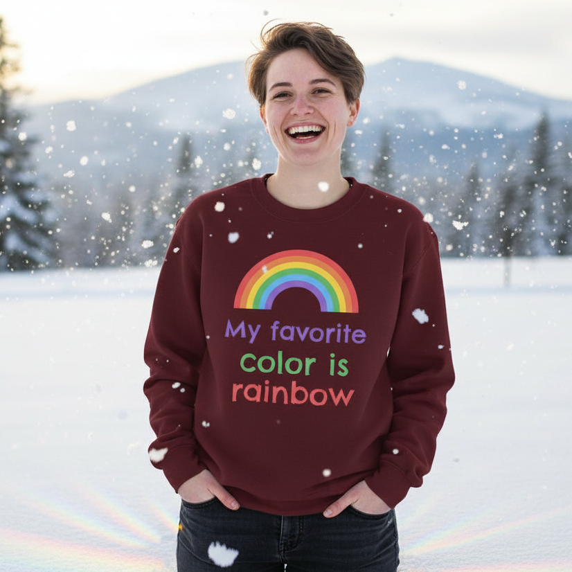 Person outdoors in snow, wearing My Favorite Colour Is Rainbow Unisex Sweatshirt, burgundy with rainbow graphic, celebrating LGBTQIA+ pride. Smiling brightly, embodying warmth and joyful queer self-expression.