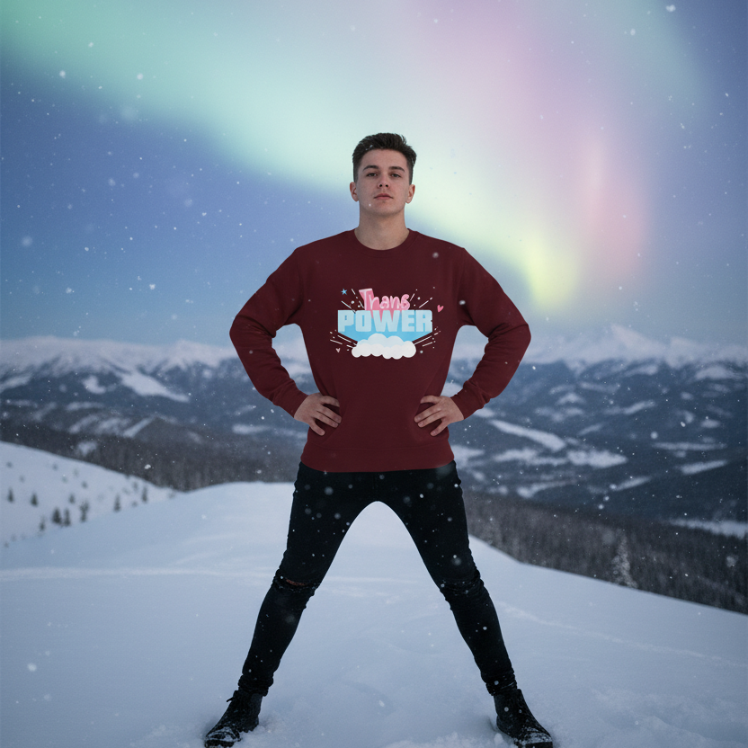 A young person confidently poses in a snowy mountain landscape, wearing the Stand Proud Trans Power Unisex Sweatshirt, showcasing playful, empowering queer pride with its bold design under the vibrant northern lights.
