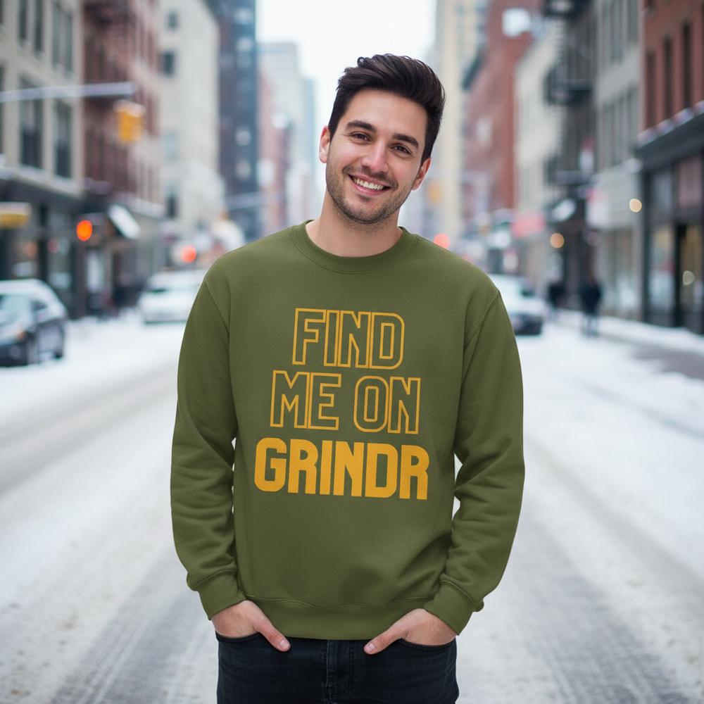 Smiling person in a green sweatshirt reading “FIND ME ON GRINDR” on a snowy city street