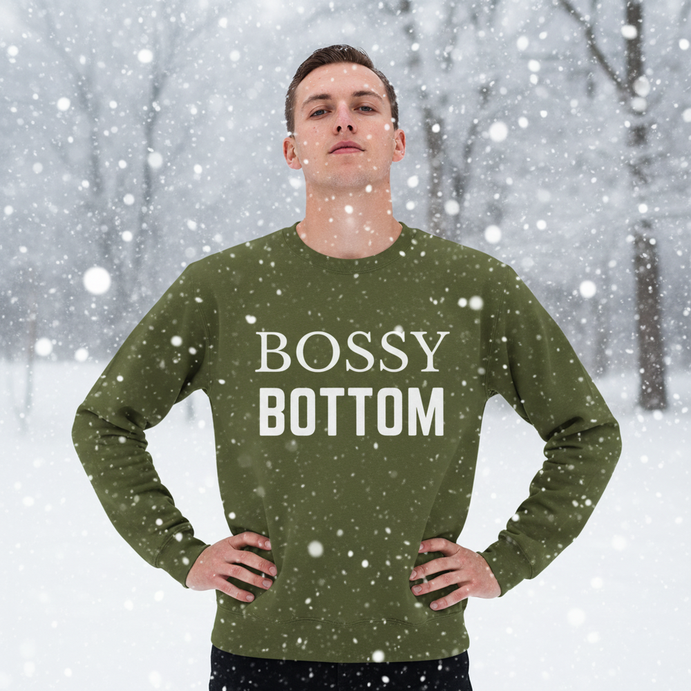 Front-facing model in falling snow wearing an olive sweatshirt reading “BOSSY BOTTOM.”