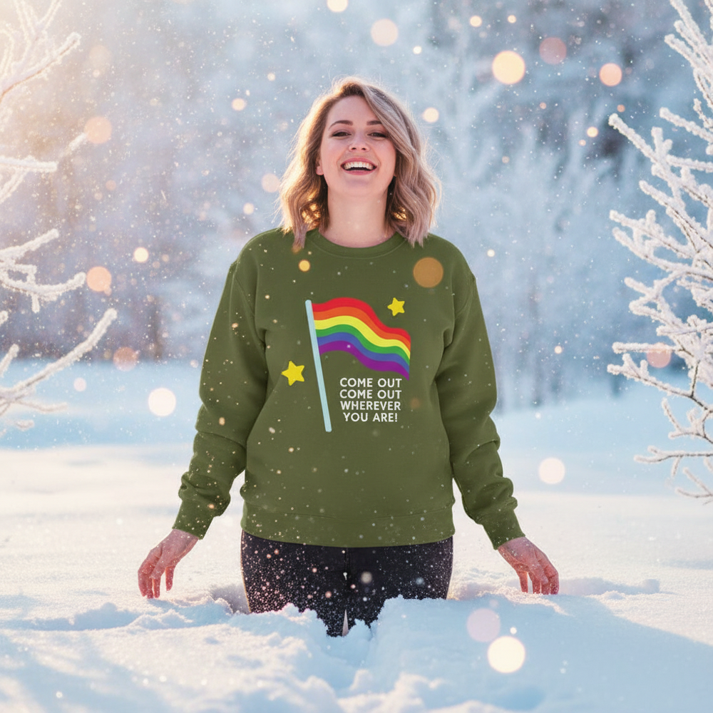 Smiling person in a green sweatshirt with a rainbow flag and “COME OUT COME OUT WHEREVER YOU ARE!” text, standing in snowy...