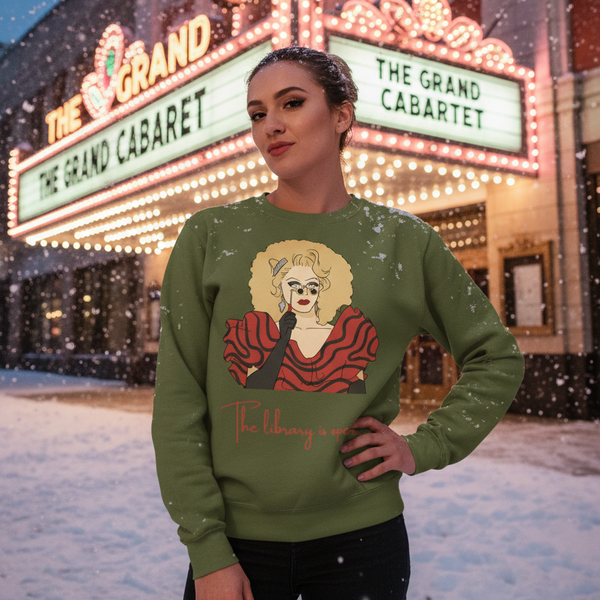 Model wearing an olive sweatshirt with a drag performer illustration and “The Library Is Open” text