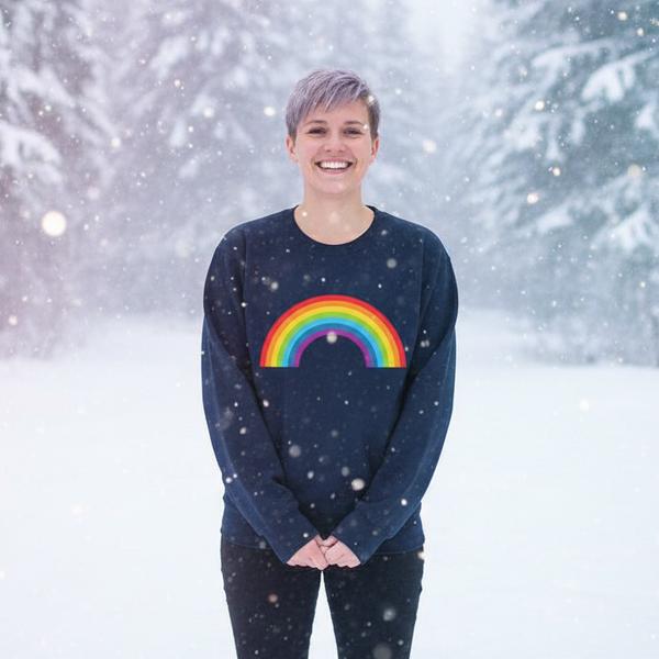 Smiling person wearing a navy sweatshirt with a rainbow graphic in falling snow