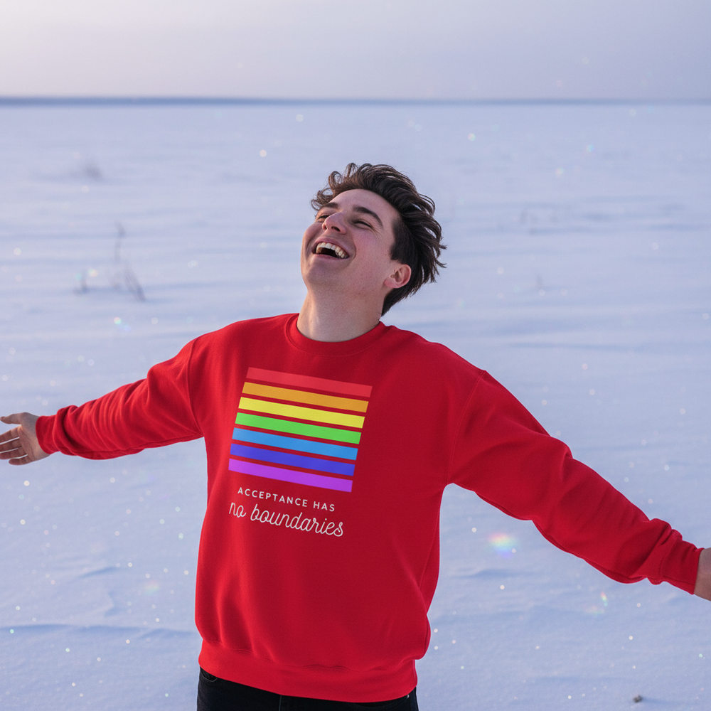 Person laughing in snow wearing a red sweatshirt with rainbow stripes and “Acceptance Has no boundaries” text