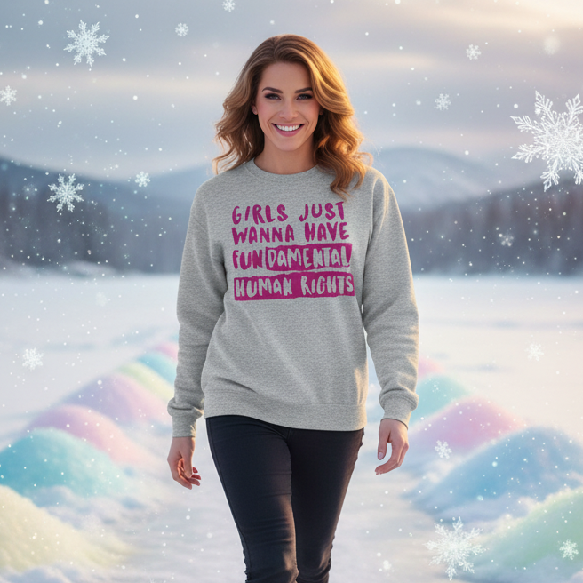 Smiling woman in a Girls Just Wanna Have Fundamental Human Rights unisex sweatshirt, showcasing LGBTQ pride. The light gray sweatshirt features bold purple lettering, embodying empowerment and self-expression amidst a snowy backdrop.