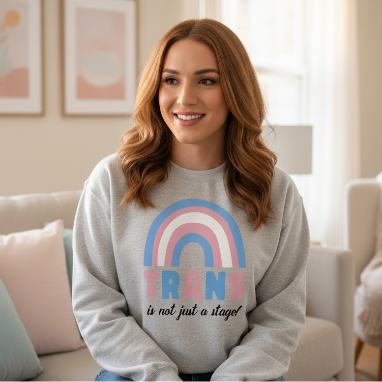 Light gray "Trans Is Not Just A Stage!'' unisex sweatshirt worn by a smiling woman, lounging on a cozy queer-friendly couch.