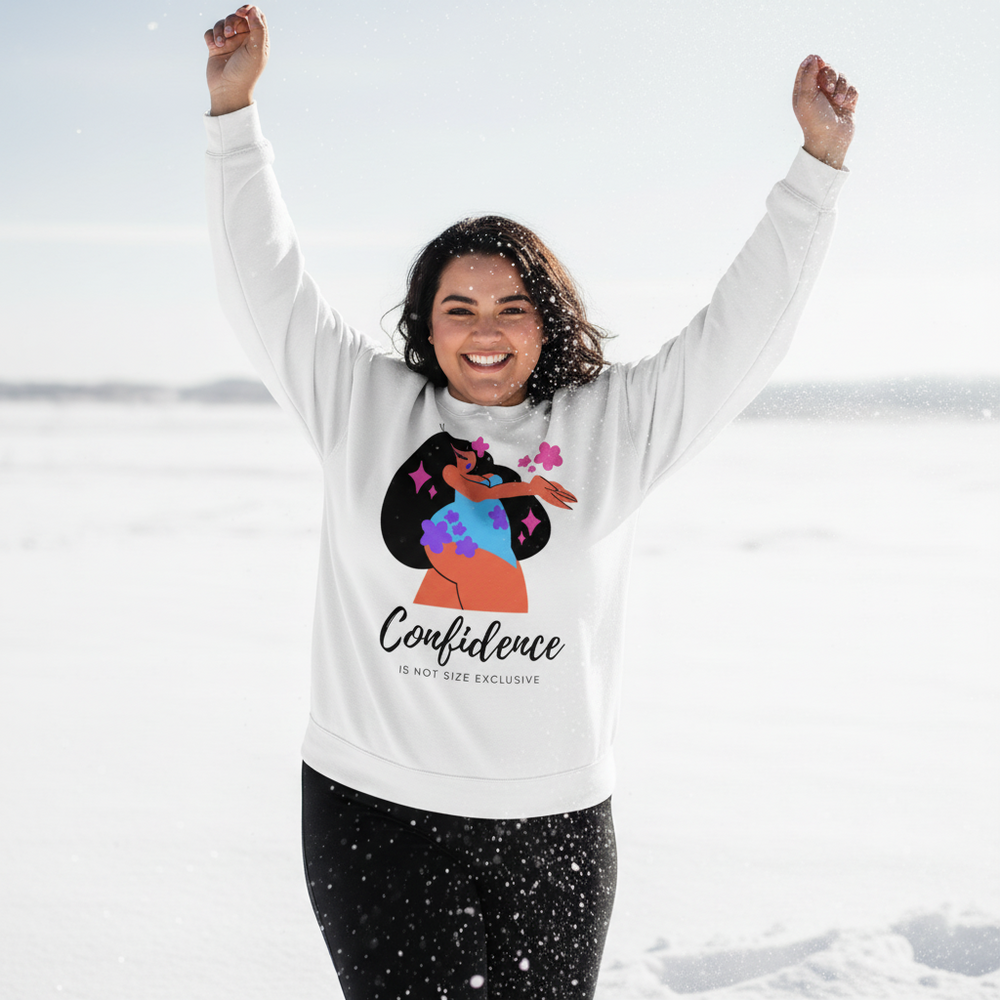 Smiling person in snow wearing a white sweatshirt reading “Confidence Is Not Size Exclusive”