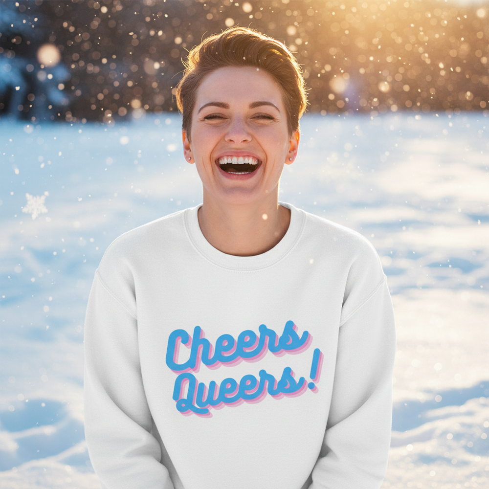Front view of a smiling person in a white sweatshirt reading “Cheers Queers!” in snow