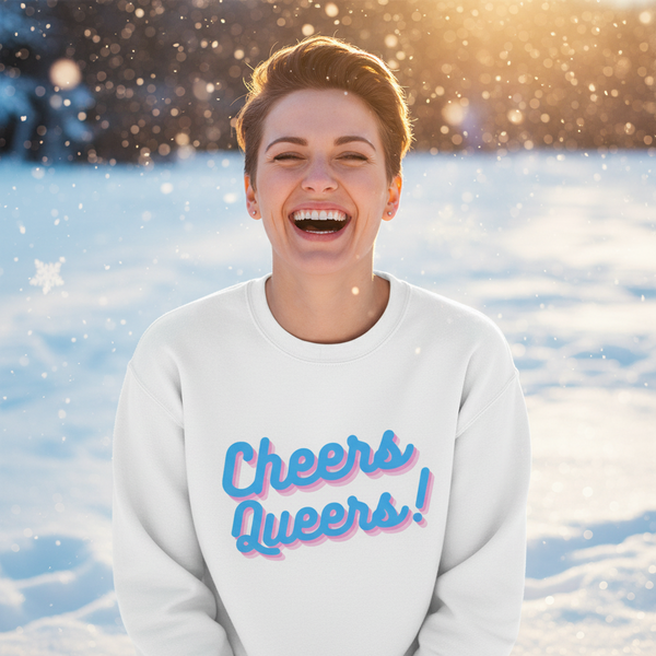 Front view of a smiling person in a white sweatshirt reading “Cheers Queers!” in snow
