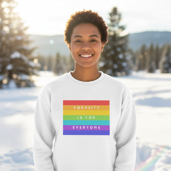 Smiling person wears a white sweatshirt with a rainbow “EQUALITY IS FOR EVERYONE” graphic in snowy woods
