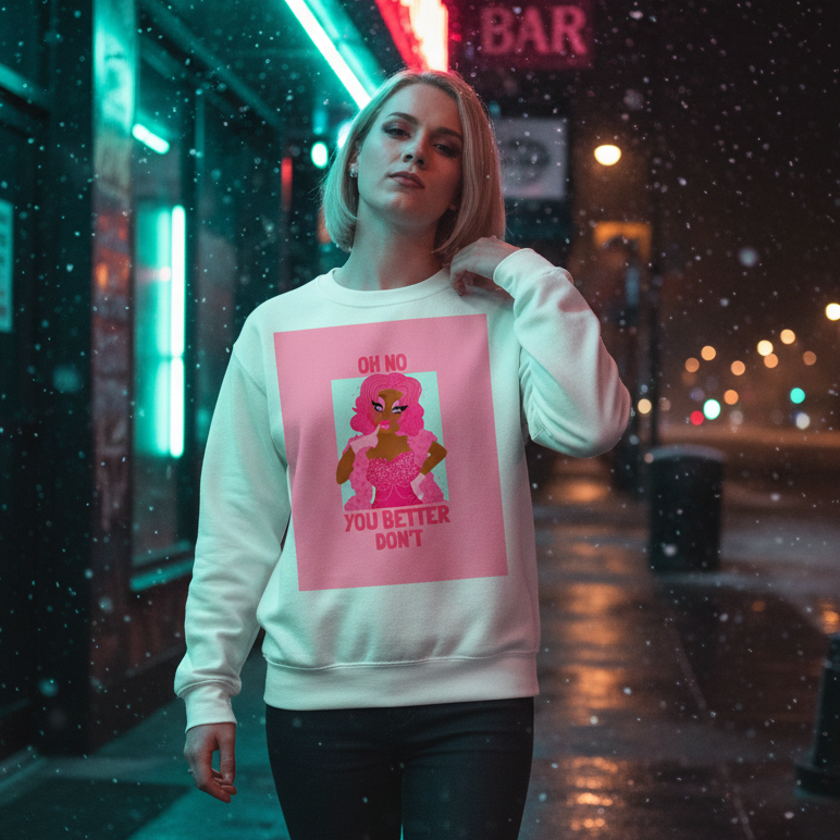 Young person proudly wearing the Oh No You Better Don't Unisex Sweatshirt with a bold pink drag-style figure graphic, standing on a vibrant, neon-lit city sidewalk at night.