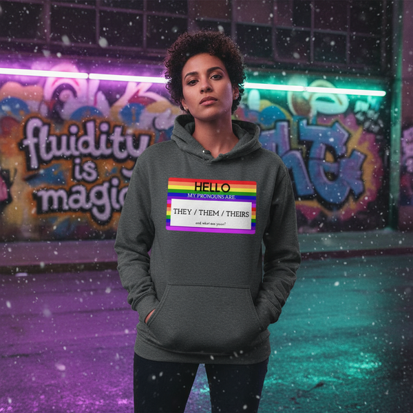 Model wearing a gray hoodie with a rainbow pronoun label reading “THEY / THEM / THEIRS”