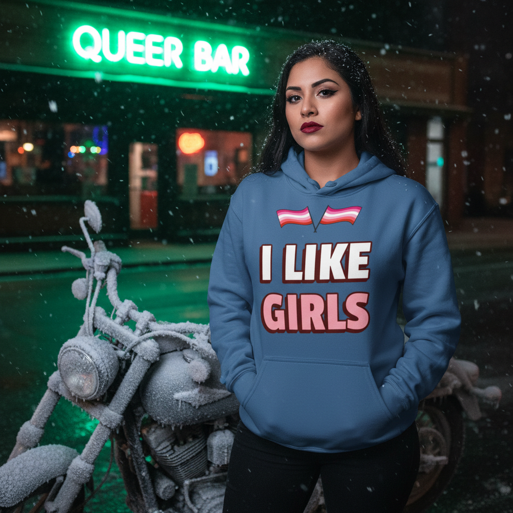 Person modeling a blue “I LIKE GIRLS” hoodie beneath two rainbow-flag icons in falling snow