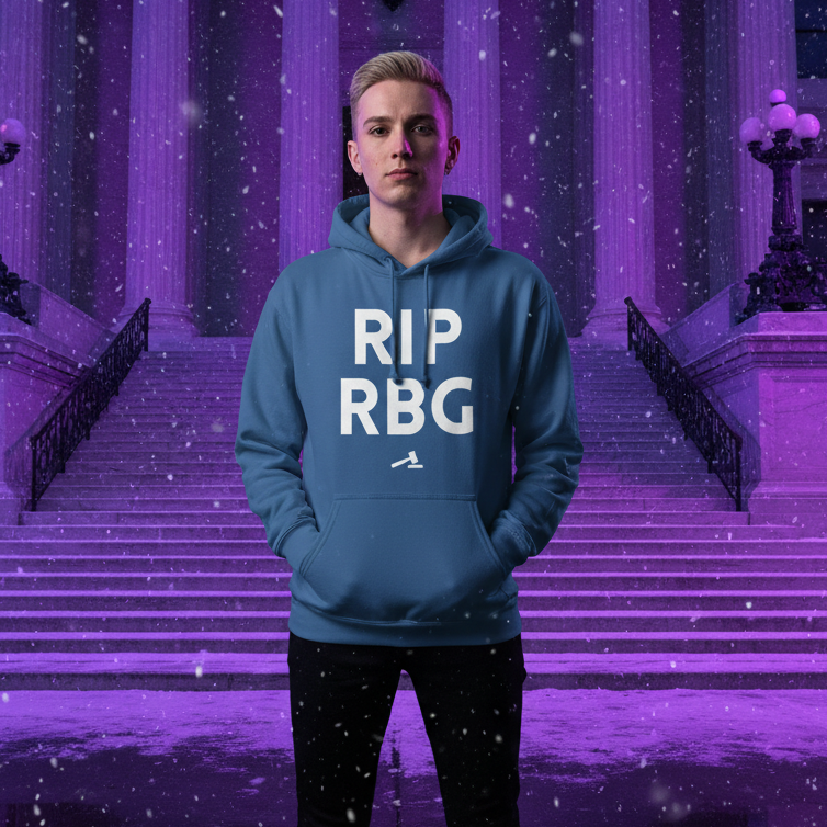 Young person in blue RIP RBG Unisex Hoodie, proudly standing before grand building. Snow falls gently, embodying queer pride and empowerment with this soft, stylish, and inclusive fashion statement.