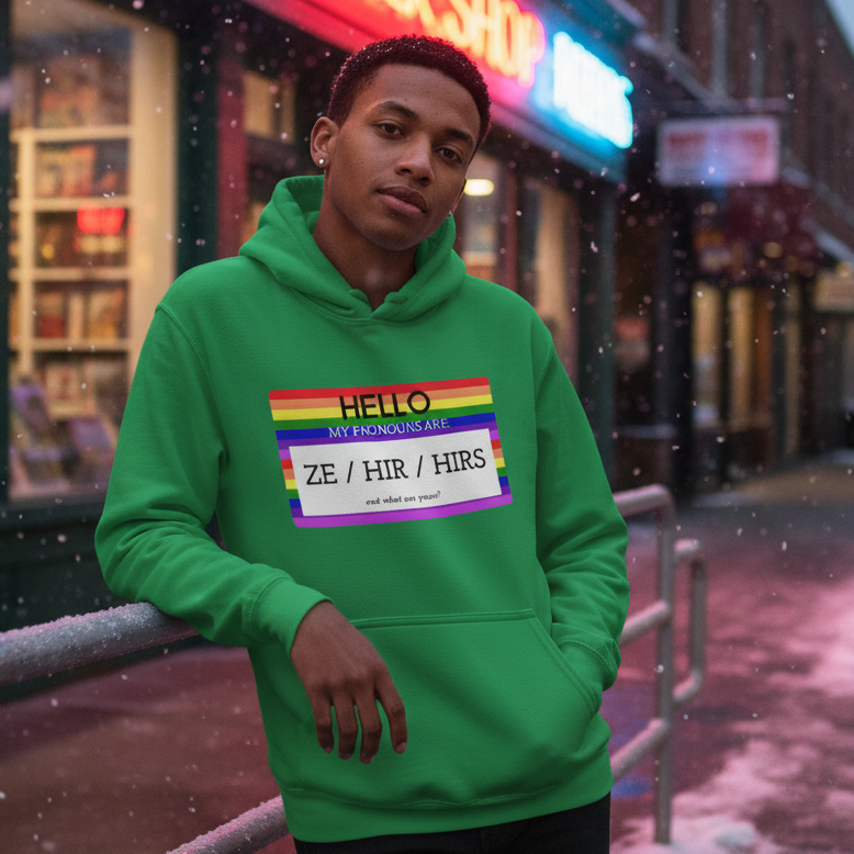 Model wearing a green hoodie with a rainbow pronoun card reading “ZE / HIR / HIRS”