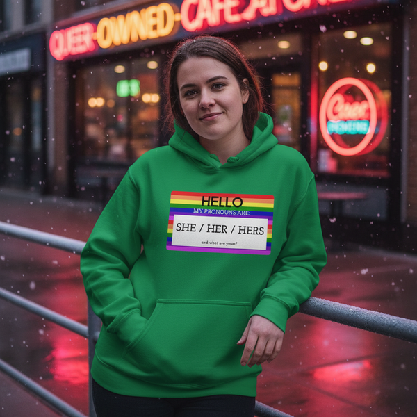 Person wearing a green hoodie with rainbow stripes and “SHE / HER / HERS” pronoun graphic