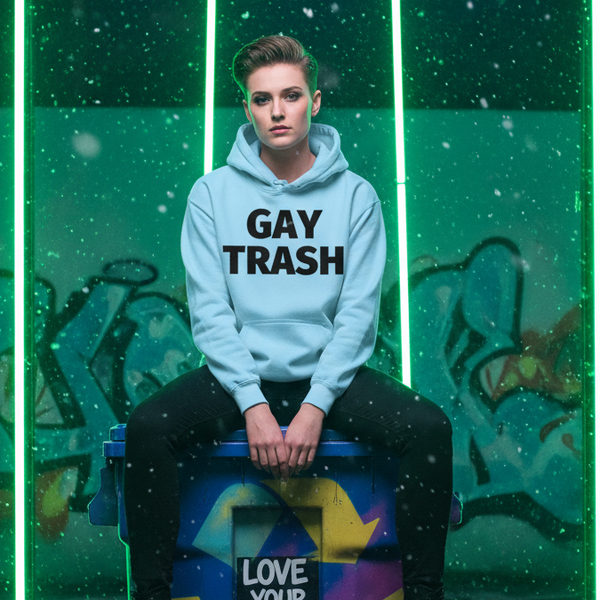 Model wearing a light blue hoodie reading “GAY TRASH” in a graffiti-lit setting