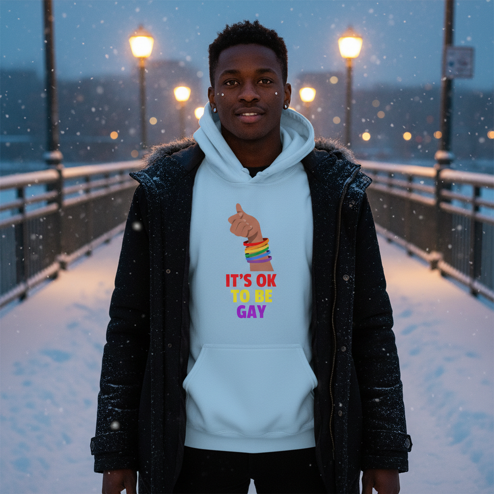 Front-facing model wears a light blue hoodie reading “IT’S OK TO BE GAY” in falling snow