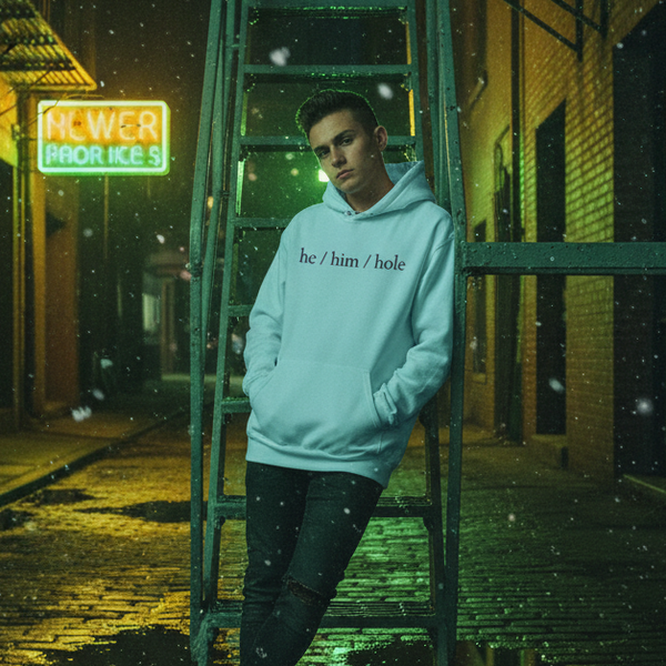 Model in a light blue hoodie reading “he / him / hole” in a rainy neon-lit alley